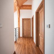 Jednoduchá chodba v patře působí čistě a harmonicky díky sladění podlahy, dveří a dřevěných trámů ve stropě.