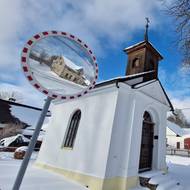 Kaplička sv. Cyrila a Metoděje na Krátké stojí hned u silnice, za níž je rozpadající se dům, který se odráží v zrcadle.
