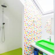 Dětská koupelna je v sytých barvách. Má atypické zelené umyvadlo, zelené dlaždičky a obklady s puntíkem.