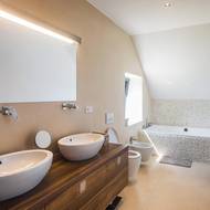 V koupelně rodičů je vana obložena přírodními kamínky. Prostoru dodává jemnou strukturu a klidnou, nadčasovou atmosféru.