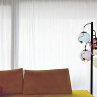 Pohovku v obývacím pokoji, která má barvu hořčice, doplňuje stojací lampa výrazných tvarů.