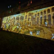 Démoni vykukují z obřího plátna a provokují návštěvníky k interakci - zásahu pomocí pěnových míčků. Instalace u řeky Mže pochází od umělecké skupiny Initi Interactive.