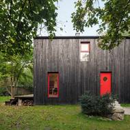 Výrazné červené prvky oživují opalovanou dřevěnou fasádu stavby.